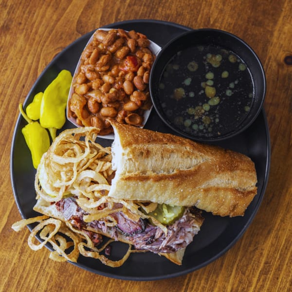 BBQ brisket sandwich with crispy onions, pickles, baked beans, and a side of au jus.