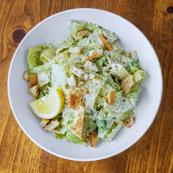 Overhead view of a Caesar salad with croutons, parmesan, and a lemon wedge in a white bowl.
