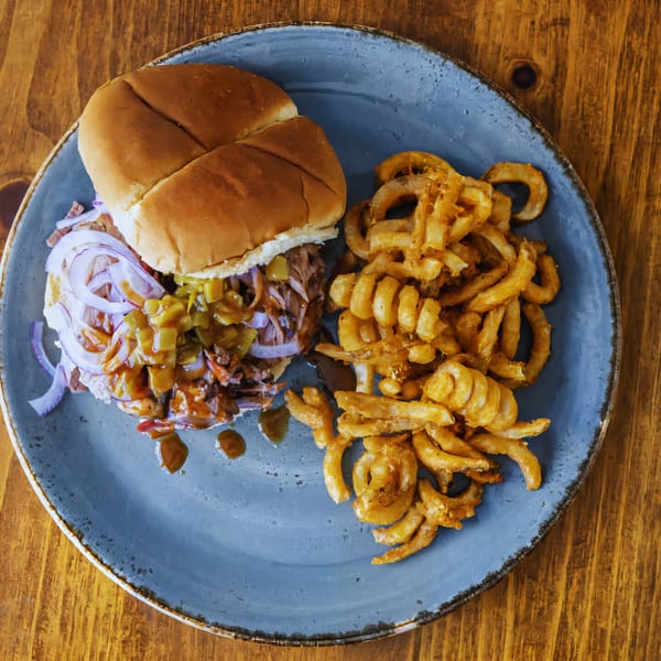 A Smoke Point BBQ pulled pork sandwich with red onions and relish, served with curly fries.