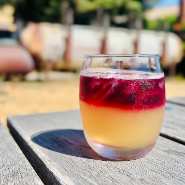 A vibrant two-toned cocktail, yellow on the bottom and red on top, sits on a wooden table.