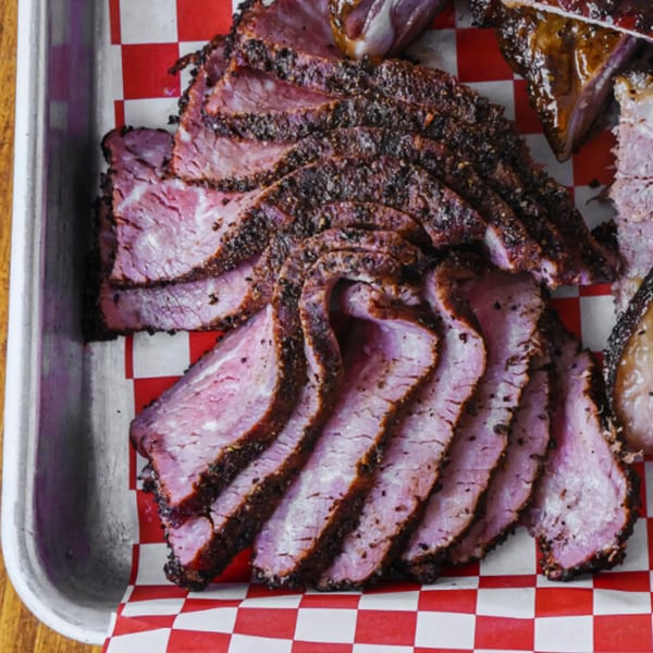 Close-up of sliced smoked brisket with a dark bark, served on red and white checkered paper.