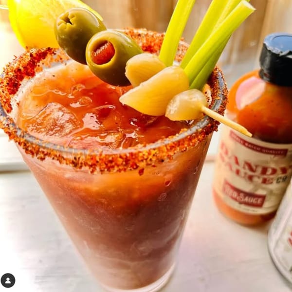 A Bloody Mary cocktail with a spicy rim, olives, pickled garlic, celery, and a lemon wedge.