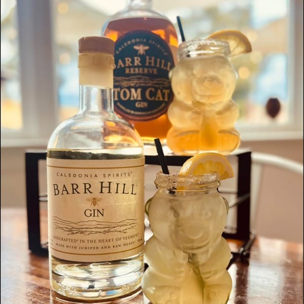 Two Barr Hill gin bottles and two honey bear-shaped cocktails with lemon slices and straws.