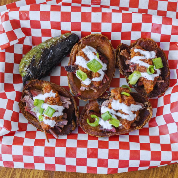 Four loaded potato skins with pulled pork, sauce, and green onions, with a charred pepper.